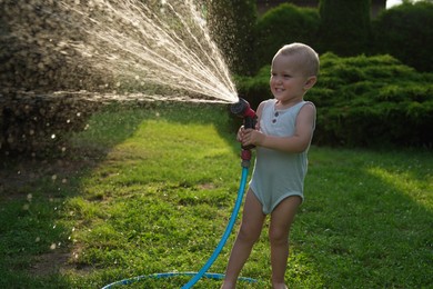 Little boy watering lawn with hose in backyard