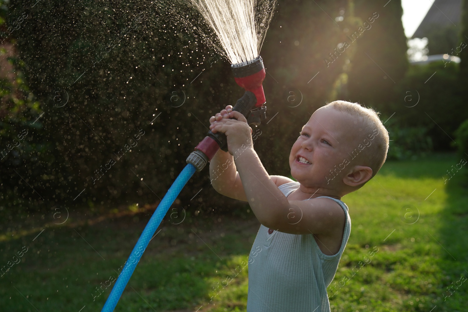 Photo of Little boy watering lawn with hose in backyard