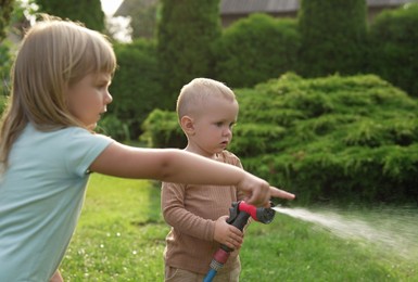 Photo of Little boy watering lawn with hose and his sister pointing at something in backyard