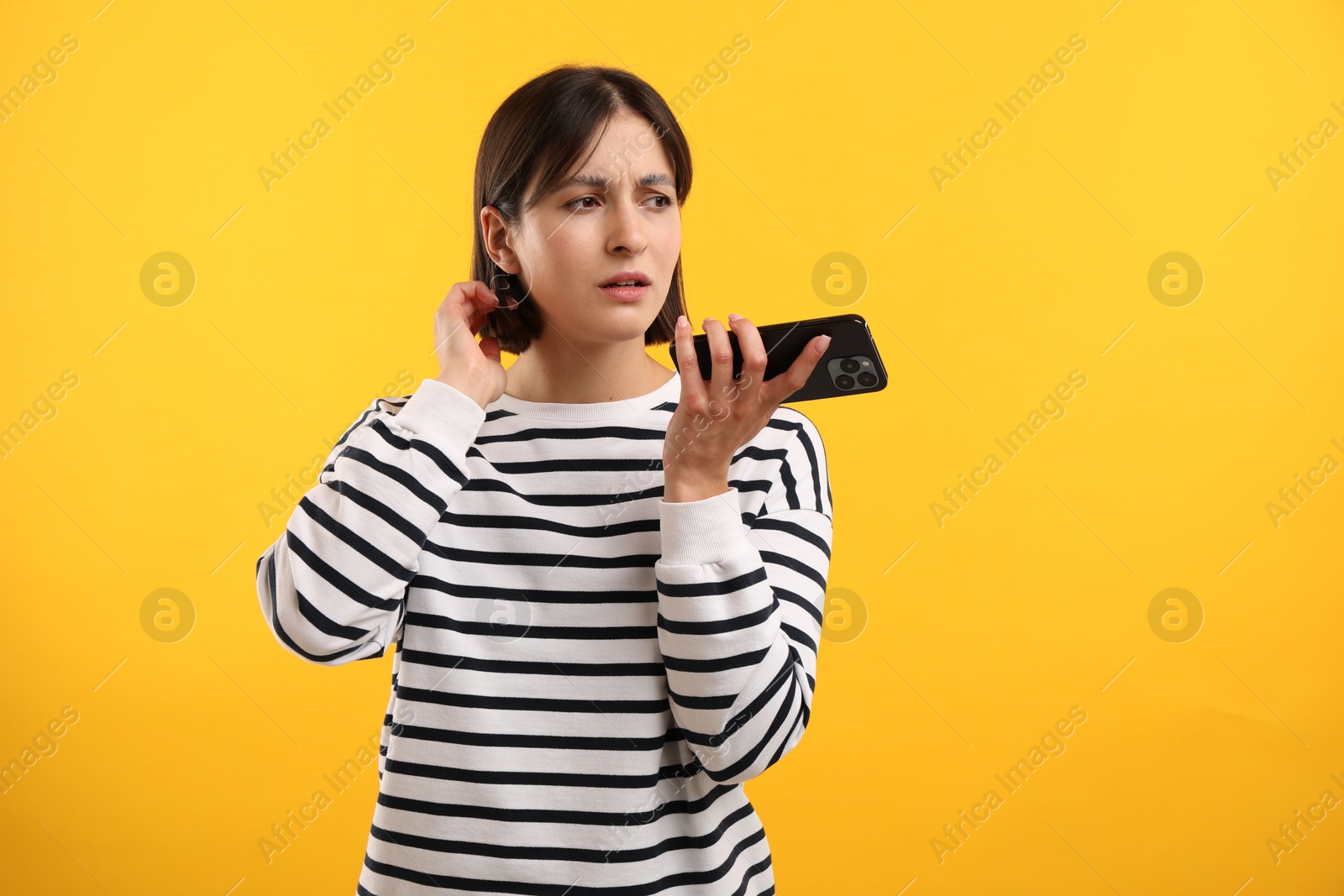 Photo of Beautiful woman recording voice message via smartphone on yellow background