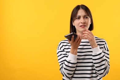 Beautiful woman recording voice message via smartphone on yellow background, space for text