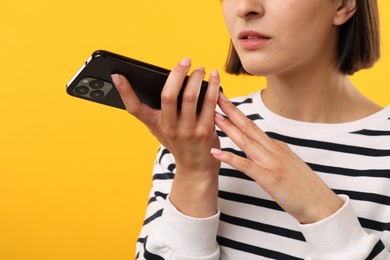 Woman recording voice message via smartphone on yellow background, closeup