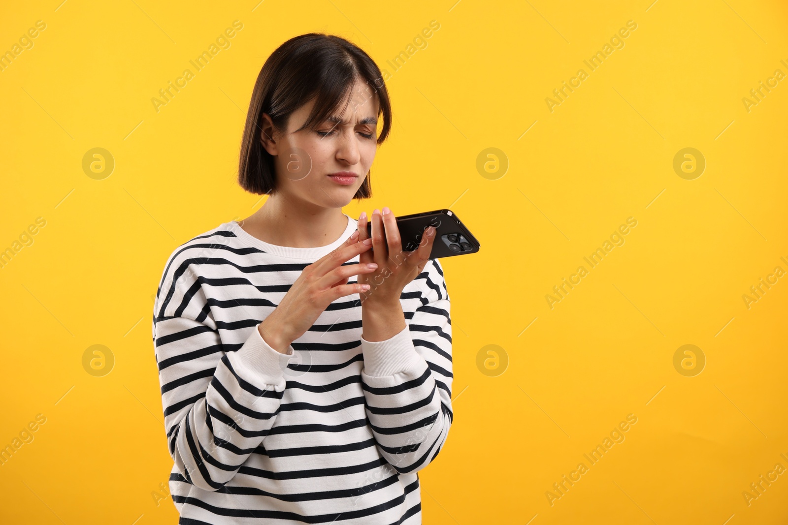 Photo of Unhappy woman recording voice message via smartphone on yellow background, space for text