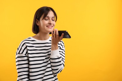 Beautiful woman recording voice message via smartphone on yellow background, space for text