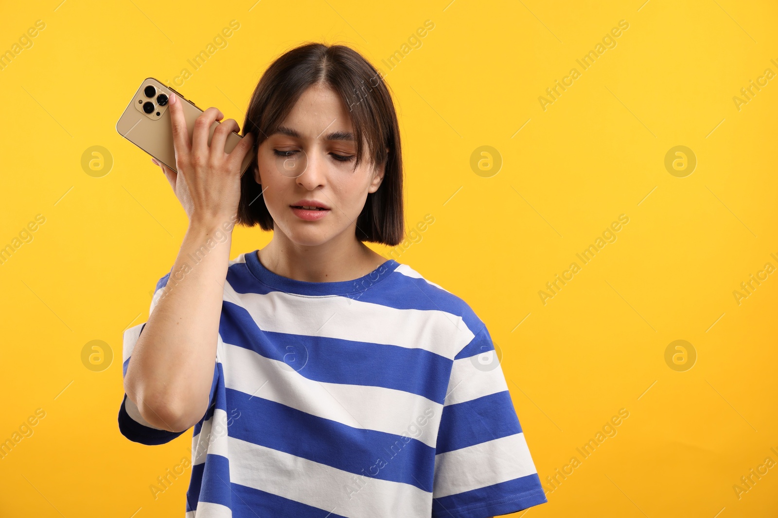 Photo of Beautiful woman with smartphone listening to voice message on yellow background, space for text