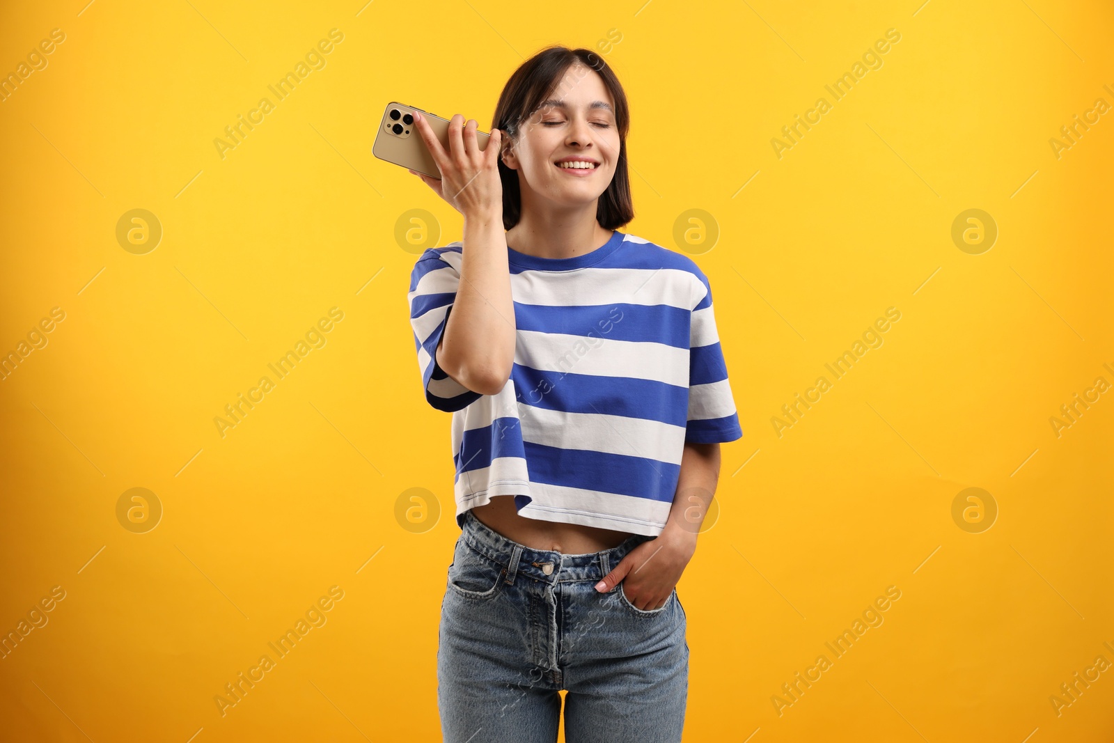 Photo of Beautiful woman with smartphone listening to voice message on yellow background