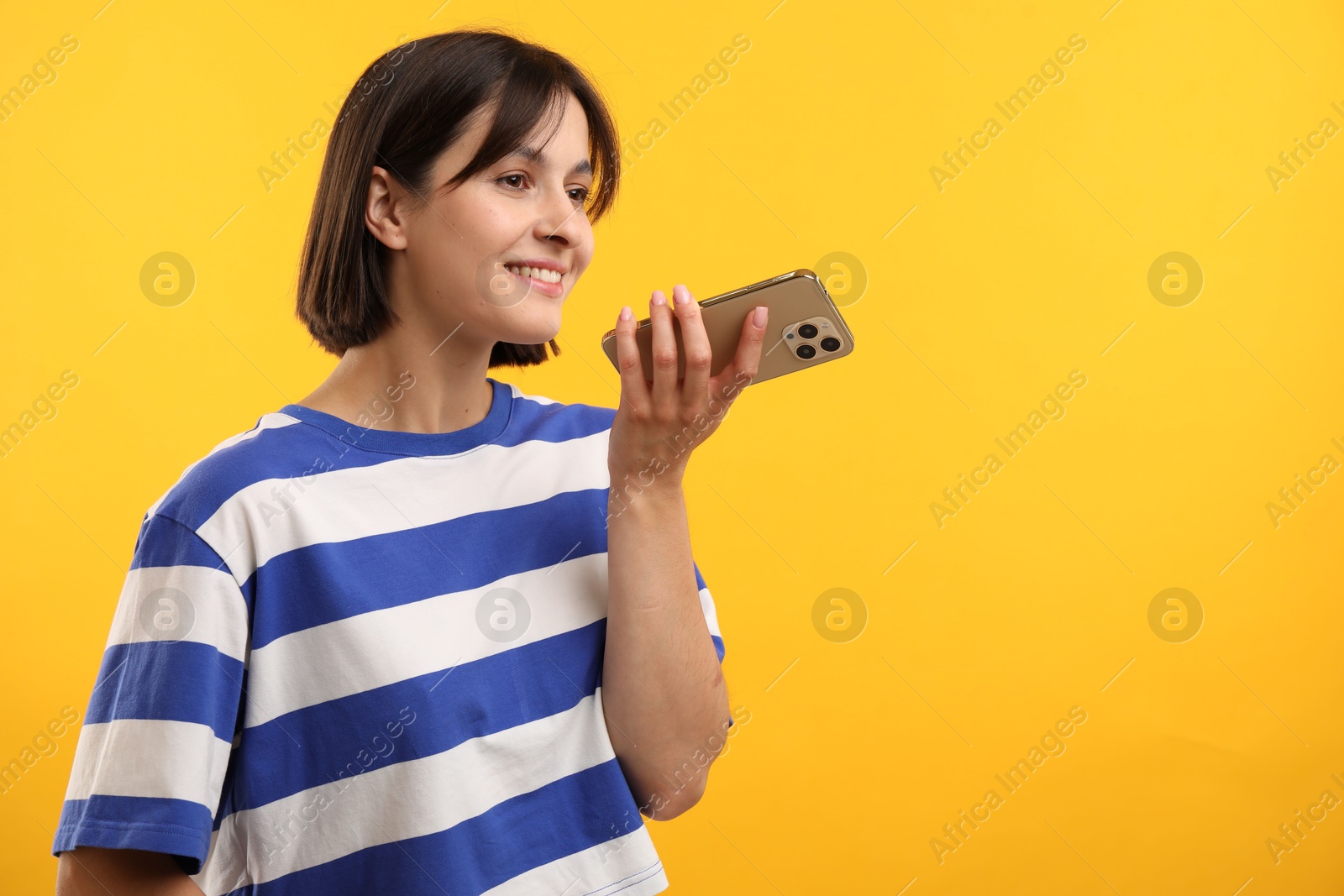 Photo of Beautiful woman recording voice message via smartphone on yellow background, space for text