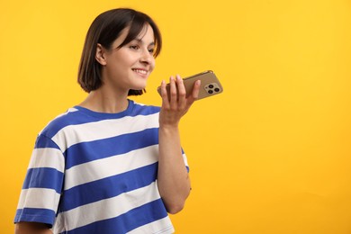 Beautiful woman recording voice message via smartphone on yellow background, space for text