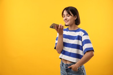 Beautiful woman recording voice message via smartphone on yellow background, space for text