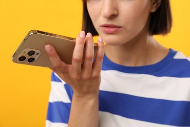 Woman recording voice message via smartphone on yellow background, closeup