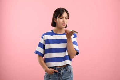 Photo of Beautiful woman recording voice message via smartphone on pink background