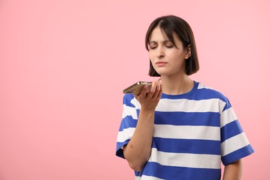 Photo of Beautiful woman recording voice message via smartphone on pink background, space for text