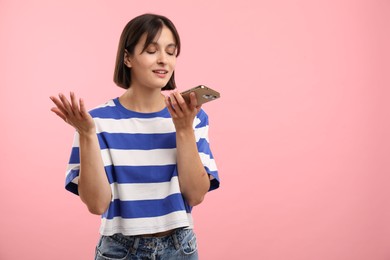 Photo of Beautiful woman recording voice message via smartphone on pink background, space for text