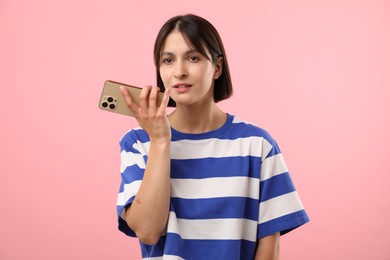 Photo of Beautiful woman recording voice message via smartphone on pink background