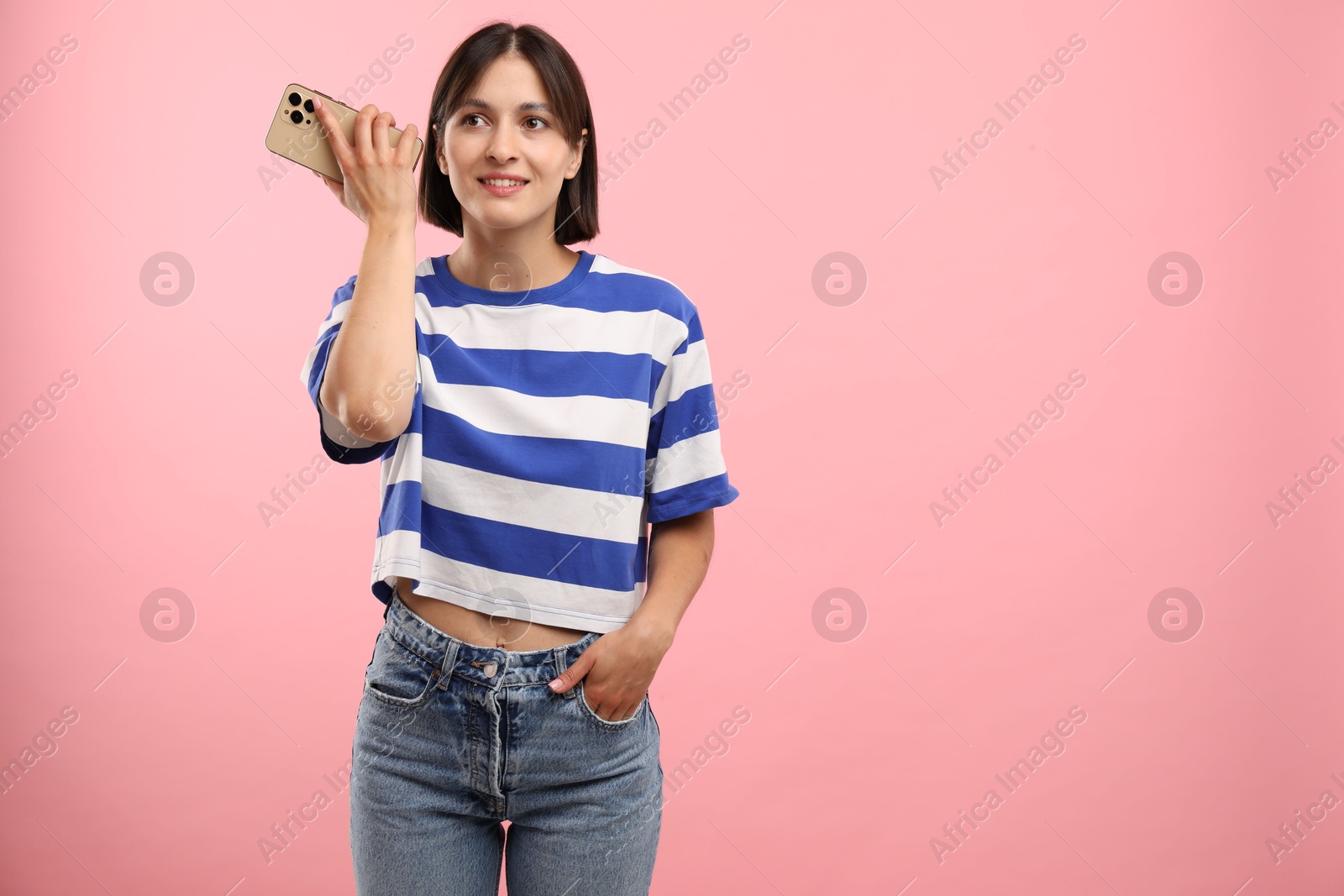 Photo of Beautiful woman with smartphone listening to voice message on pink background, space for text