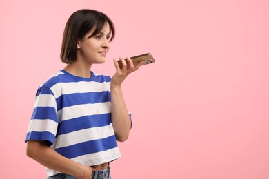 Photo of Beautiful woman recording voice message via smartphone on pink background, space for text