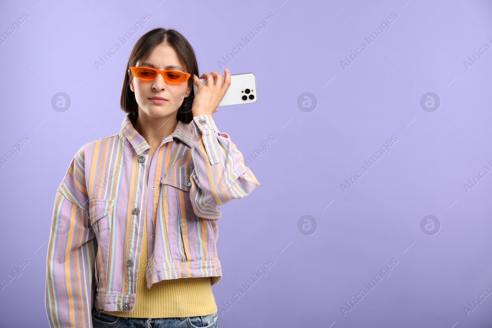 Photo of Beautiful woman in sunglasses with smartphone listening to voice message on violet background, space for text