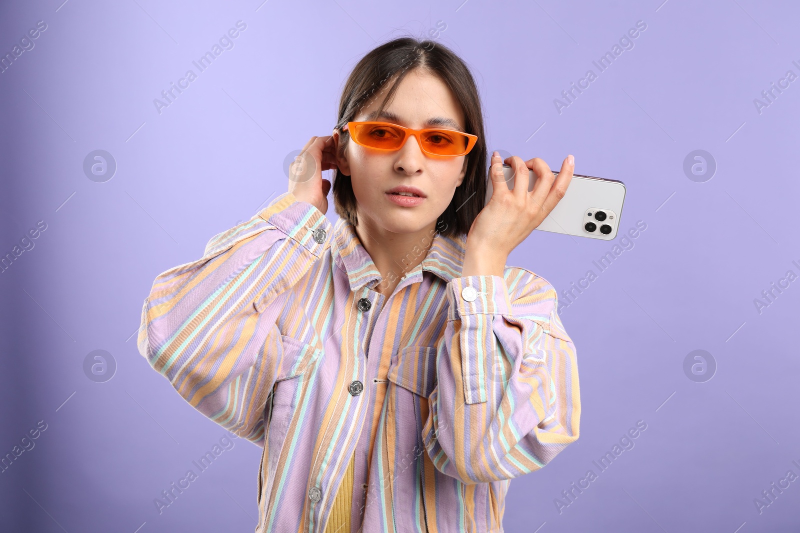 Photo of Beautiful woman in sunglasses with smartphone listening to voice message on violet background