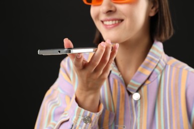 Woman recording voice message via smartphone on black background, closeup