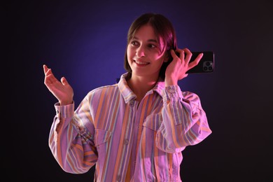 Beautiful woman listening to voice message via smartphone on dark background with neon lights