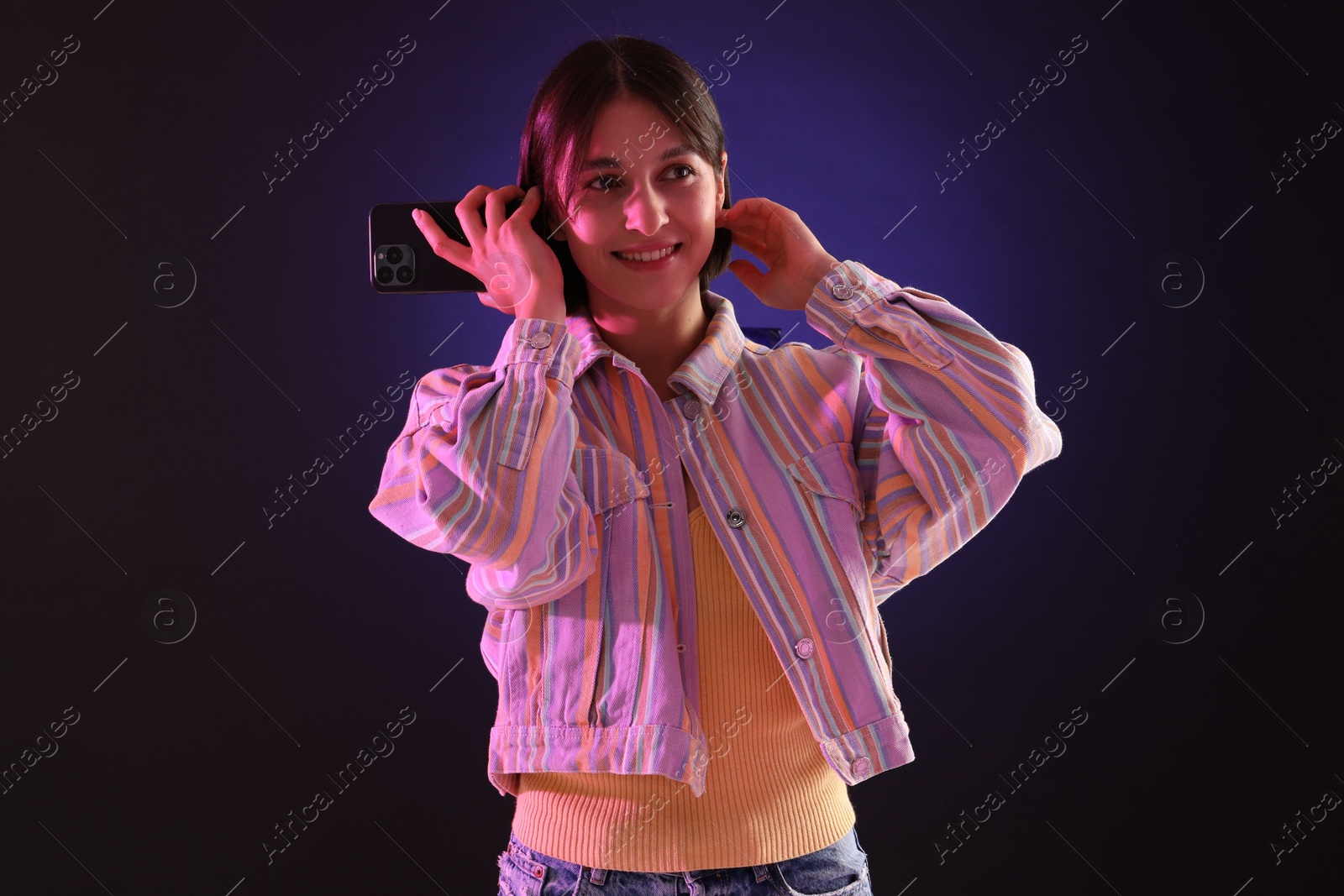 Photo of Beautiful woman listening to voice message via smartphone on dark background with neon lights