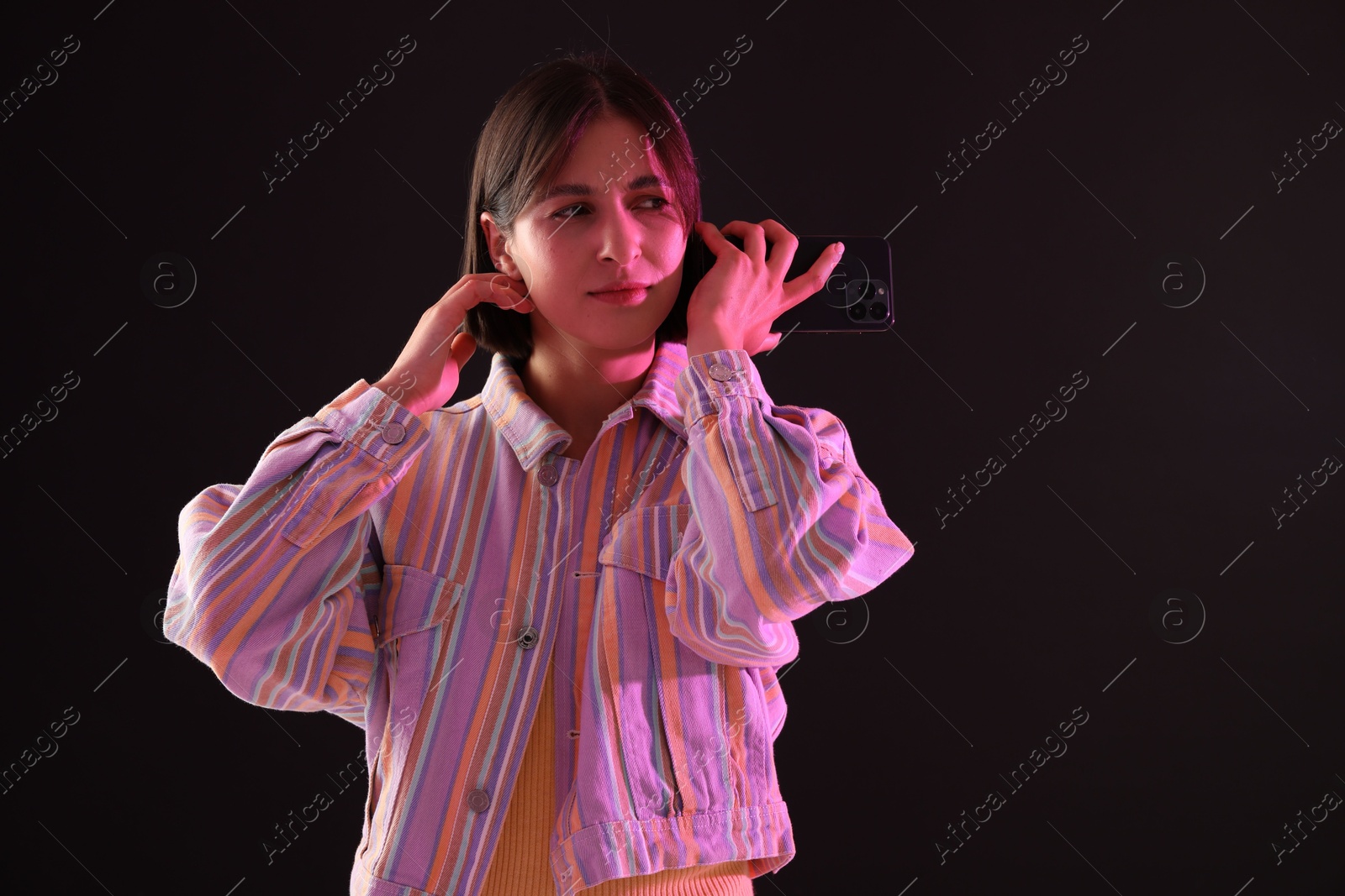 Photo of Beautiful woman listening to voice message via smartphone on dark background with neon lights