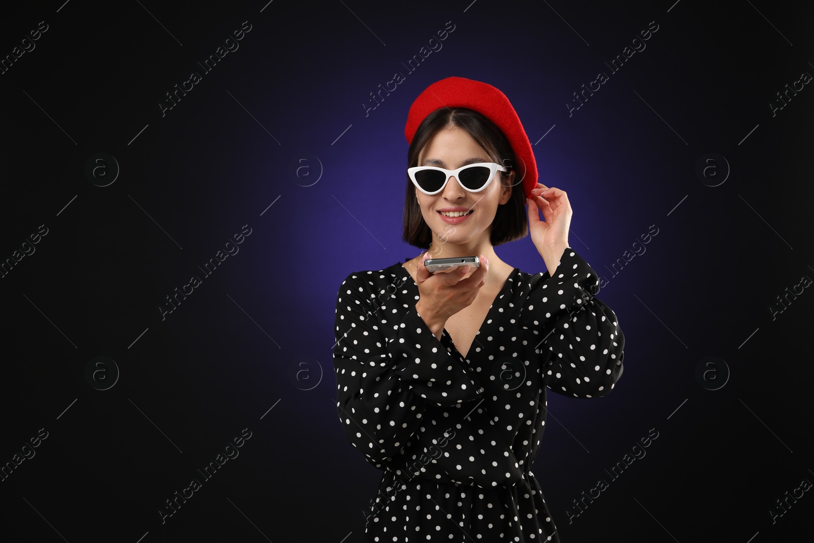 Photo of Stylish woman recording voice message via smartphone on dark background, space for text