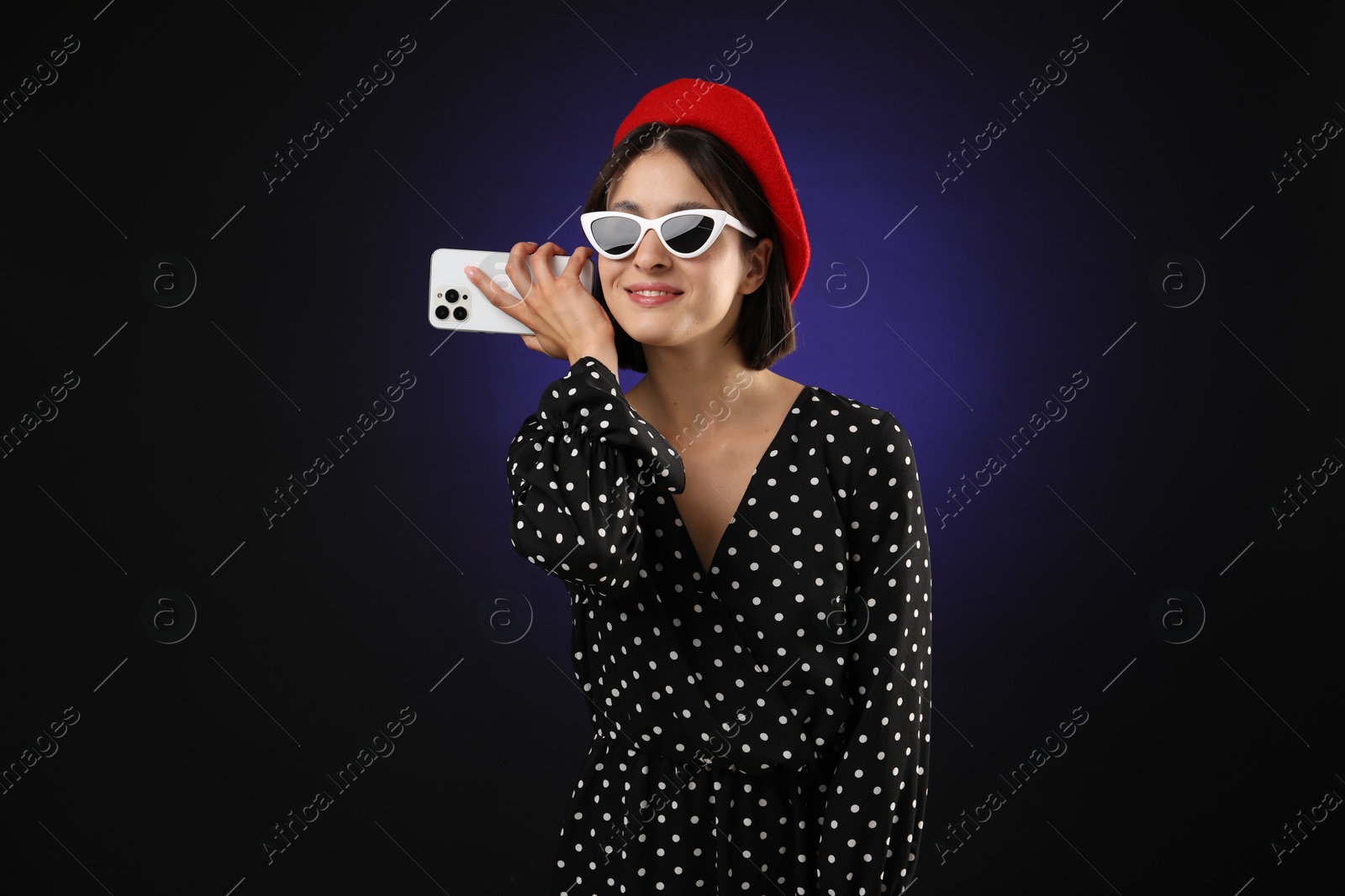 Photo of Stylish woman listening to voice message via smartphone on dark background