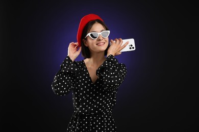 Photo of Stylish woman listening to voice message via smartphone on dark background