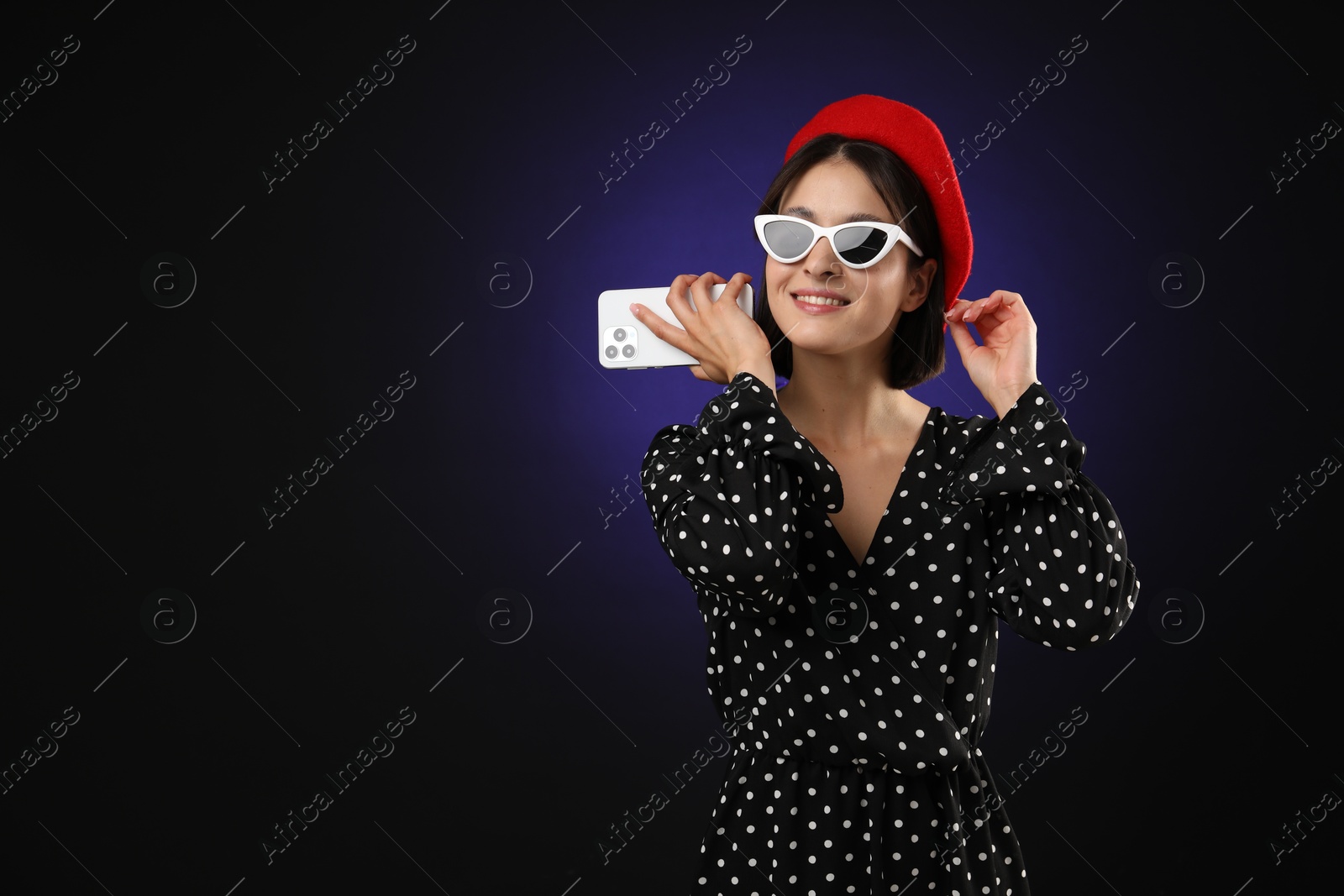 Photo of Stylish woman listening to voice message via smartphone on dark background, space for text