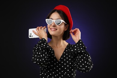 Stylish woman listening to voice message via smartphone on dark background