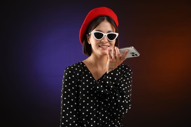 Photo of Stylish woman recording voice message via smartphone on color background