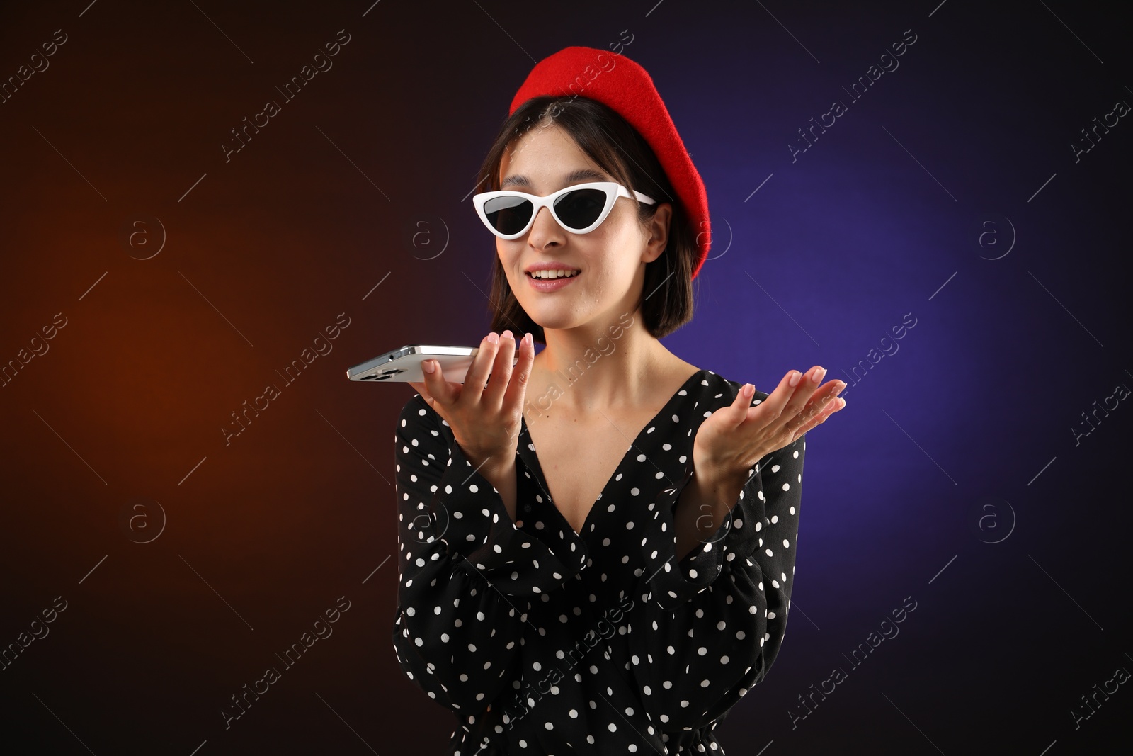 Photo of Stylish woman recording voice message via smartphone on color background