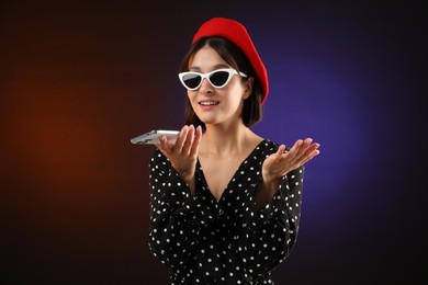 Stylish woman recording voice message via smartphone on color background