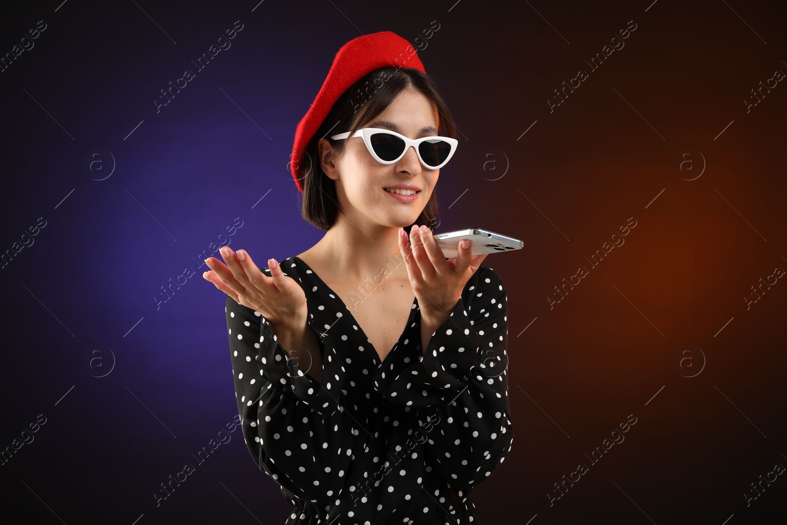 Photo of Stylish woman recording voice message via smartphone on color background