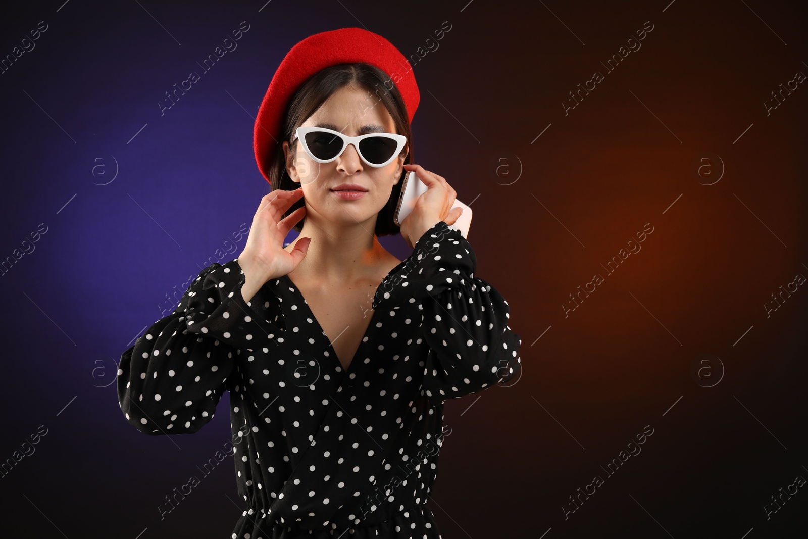 Photo of Stylish woman listening to voice message via smartphone on color background