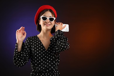 Stylish woman listening to voice message via smartphone on color background, space for text