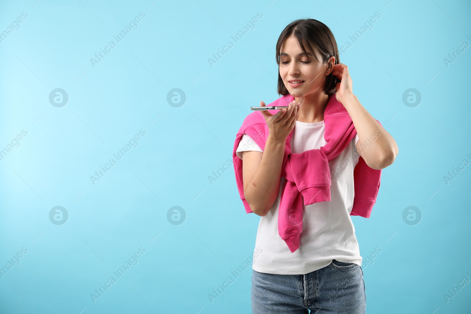 Photo of Beautiful woman recording voice message via smartphone on light blue background, space for text