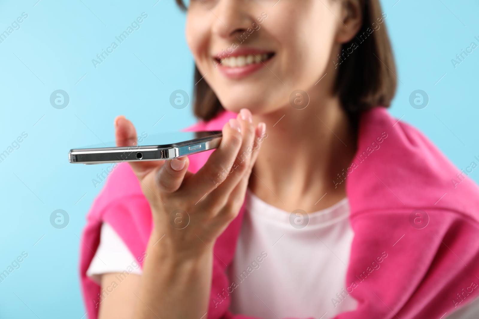 Photo of Woman recording voice message via smartphone on light blue background, closeup