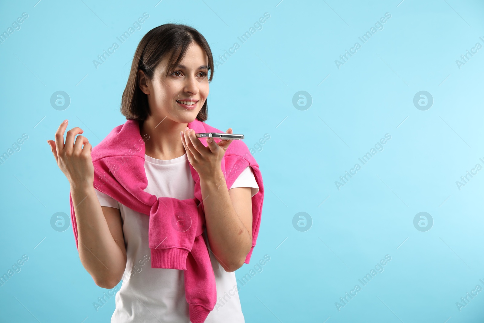 Photo of Beautiful woman recording voice message via smartphone on light blue background, space for text