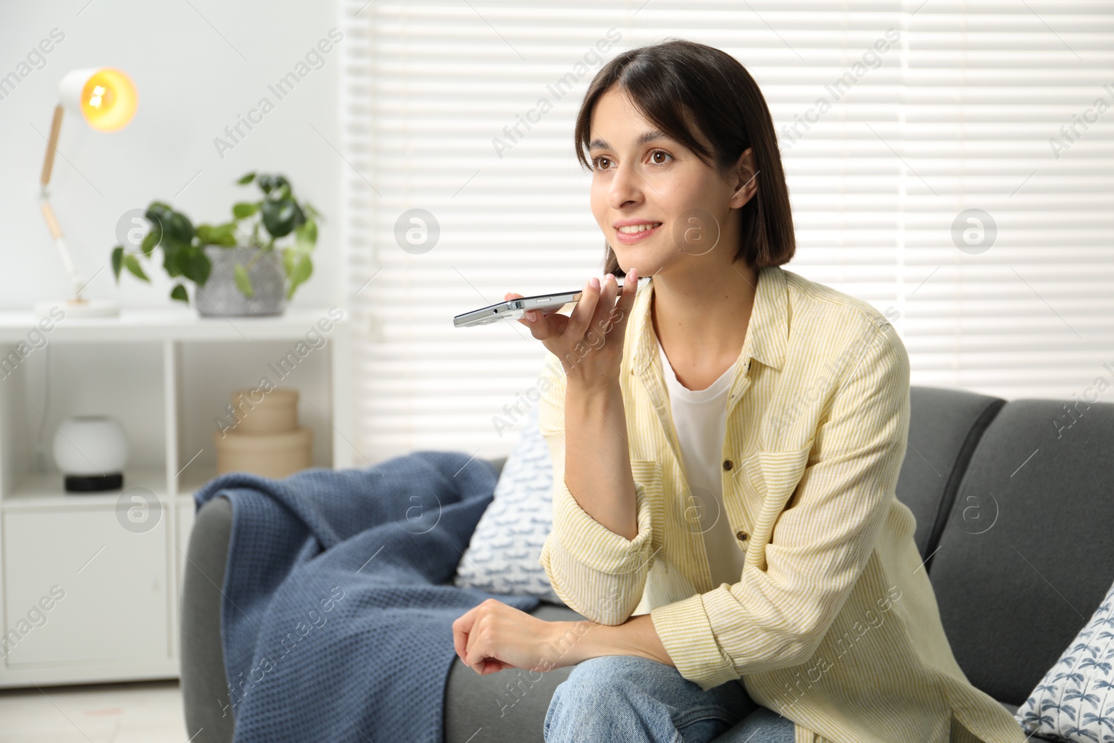 Photo of Beautiful woman recording voice message via smartphone at home