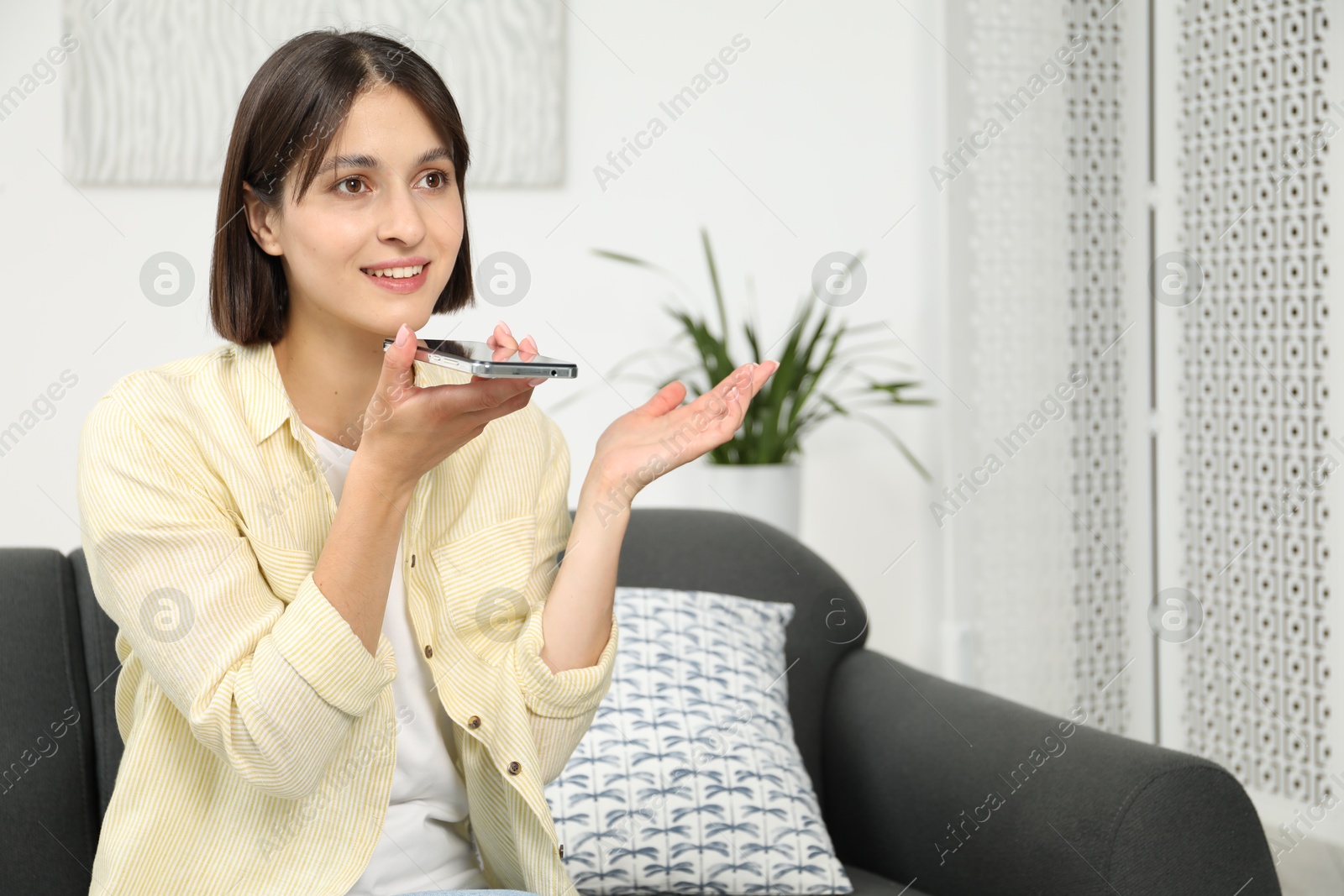 Photo of Beautiful woman recording voice message via smartphone at home