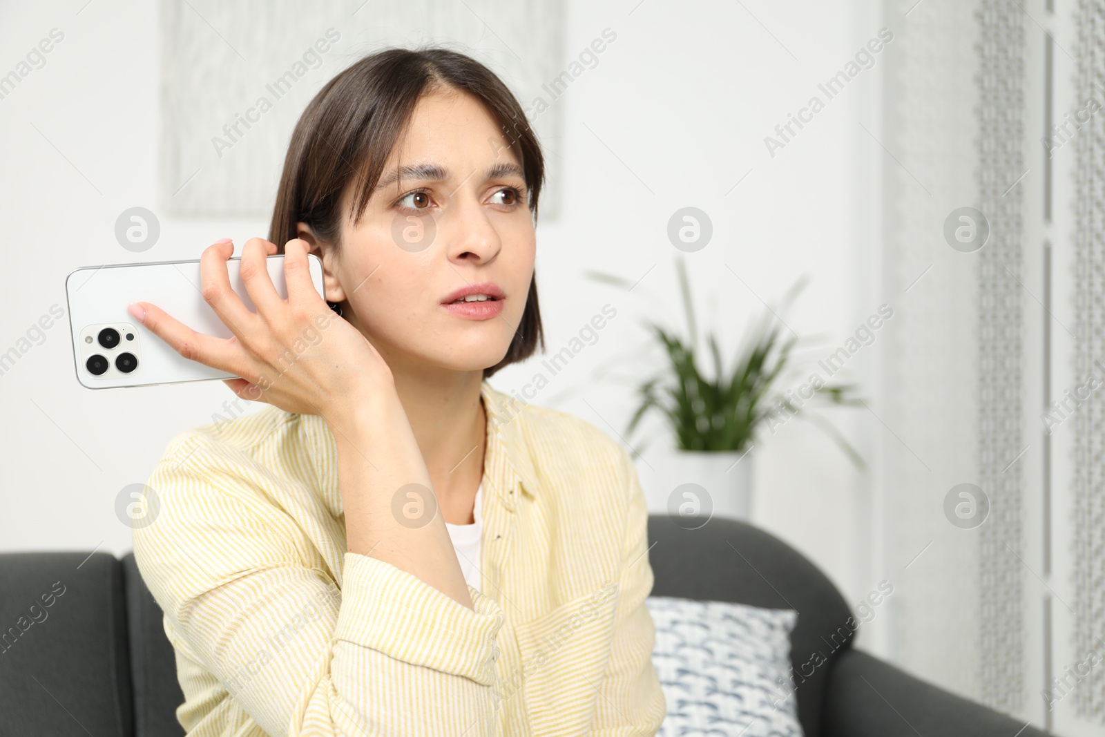 Photo of Beautiful woman with smartphone listening to voice message at home