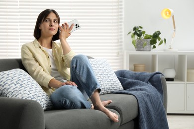 Photo of Beautiful woman with smartphone listening to voice message at home