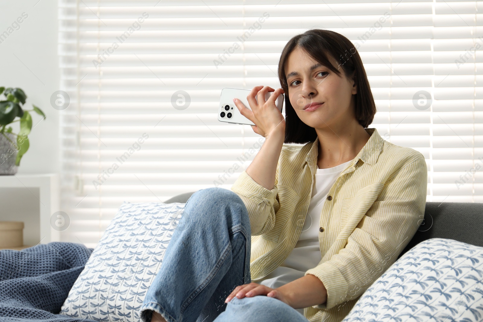 Photo of Beautiful woman with smartphone listening to voice message at home