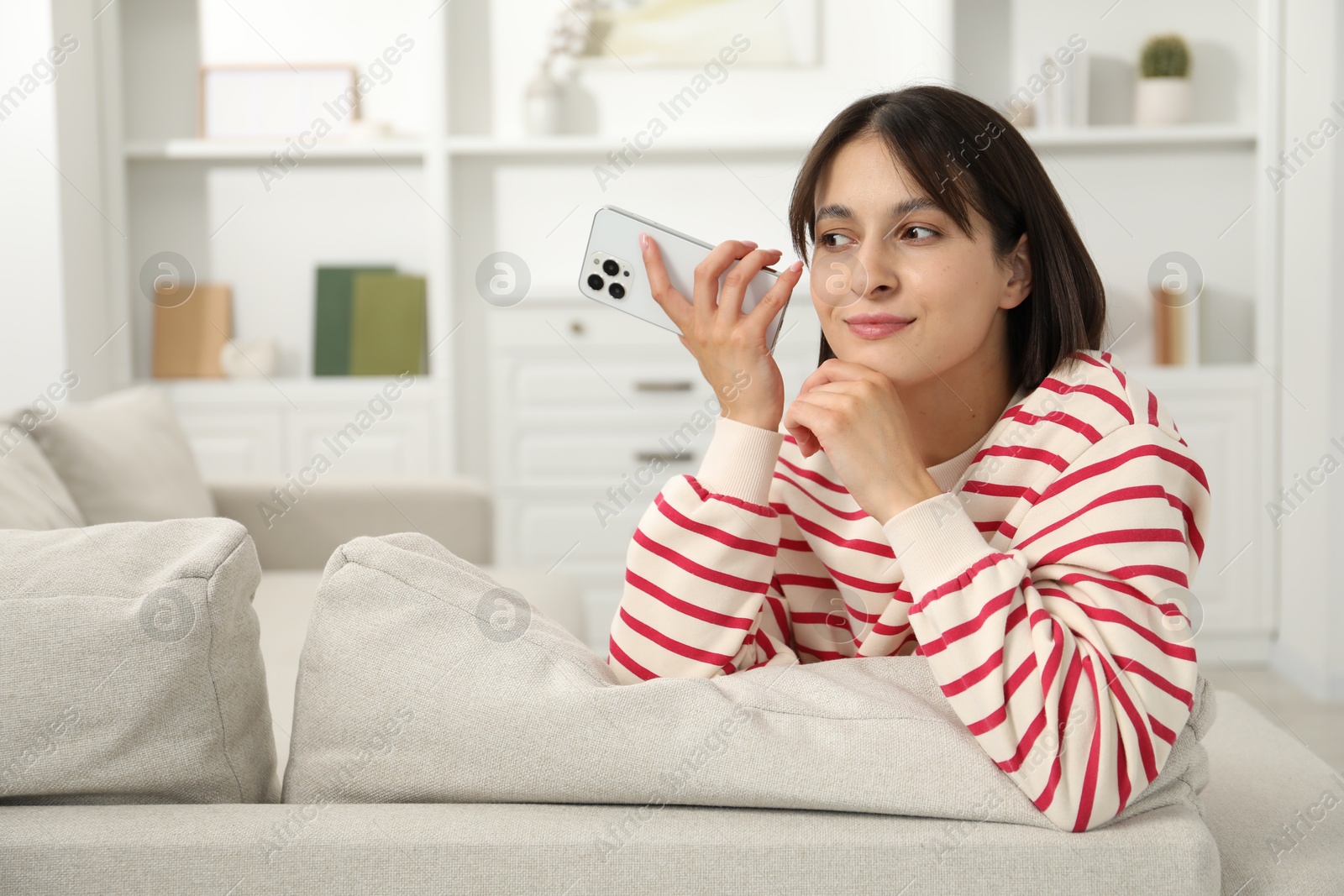 Photo of Beautiful woman with smartphone listening to voice message at home