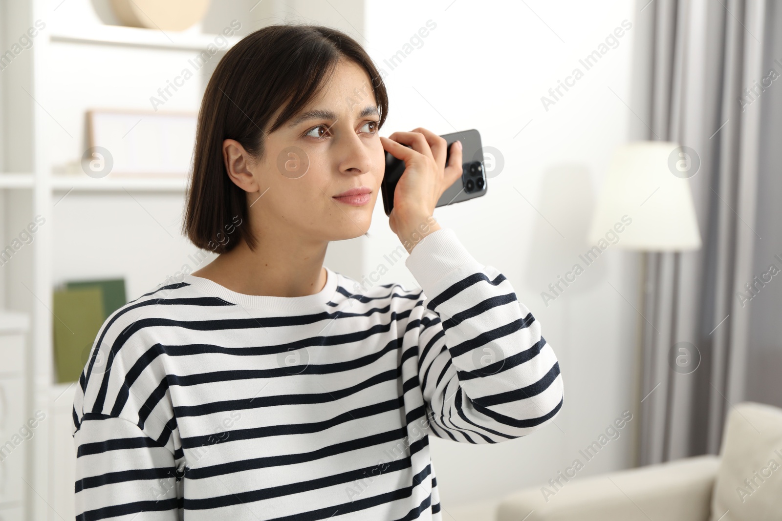 Photo of Beautiful woman with smartphone listening to voice message at home