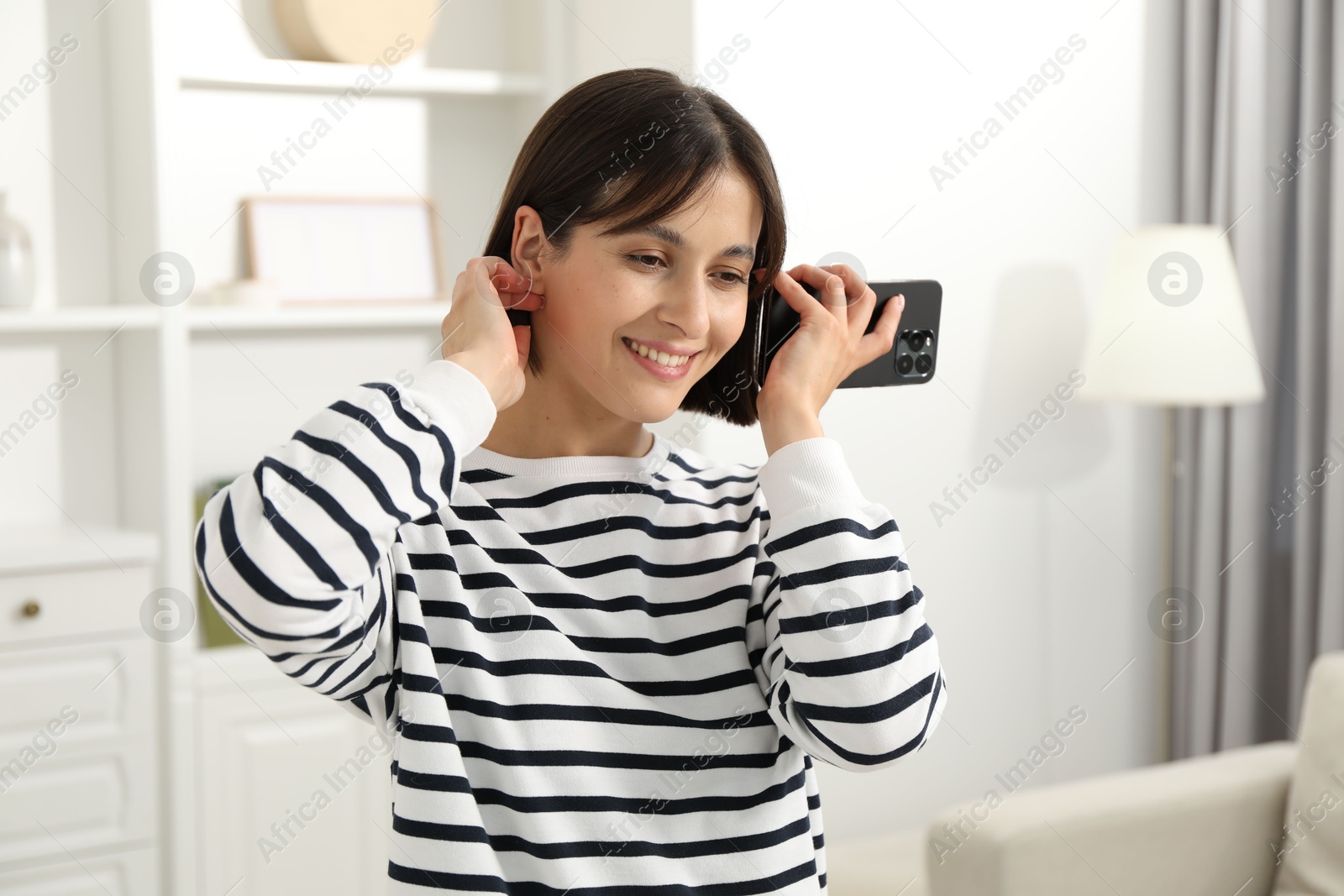 Photo of Beautiful woman with smartphone listening to voice message at home