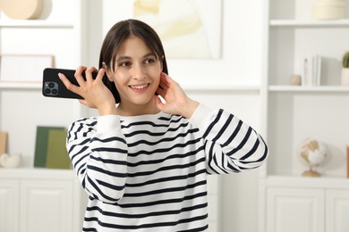 Beautiful woman with smartphone listening to voice message at home