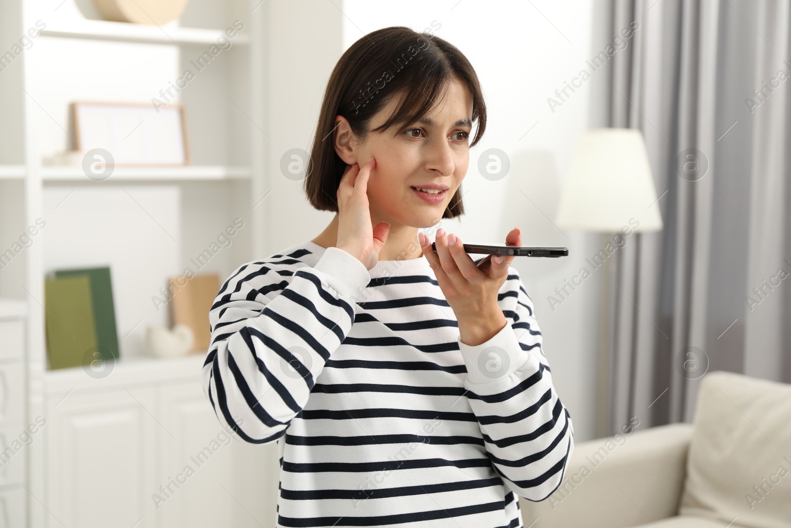 Photo of Beautiful woman recording voice message via smartphone at home